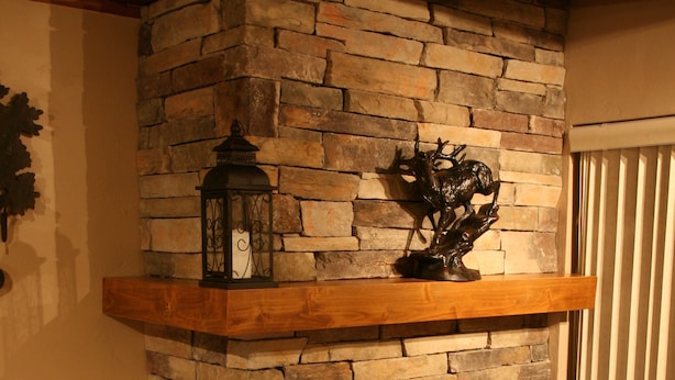 Een stenen openhaard met een houten plint, een mand vol dennenappels en een decoratief metalen object.