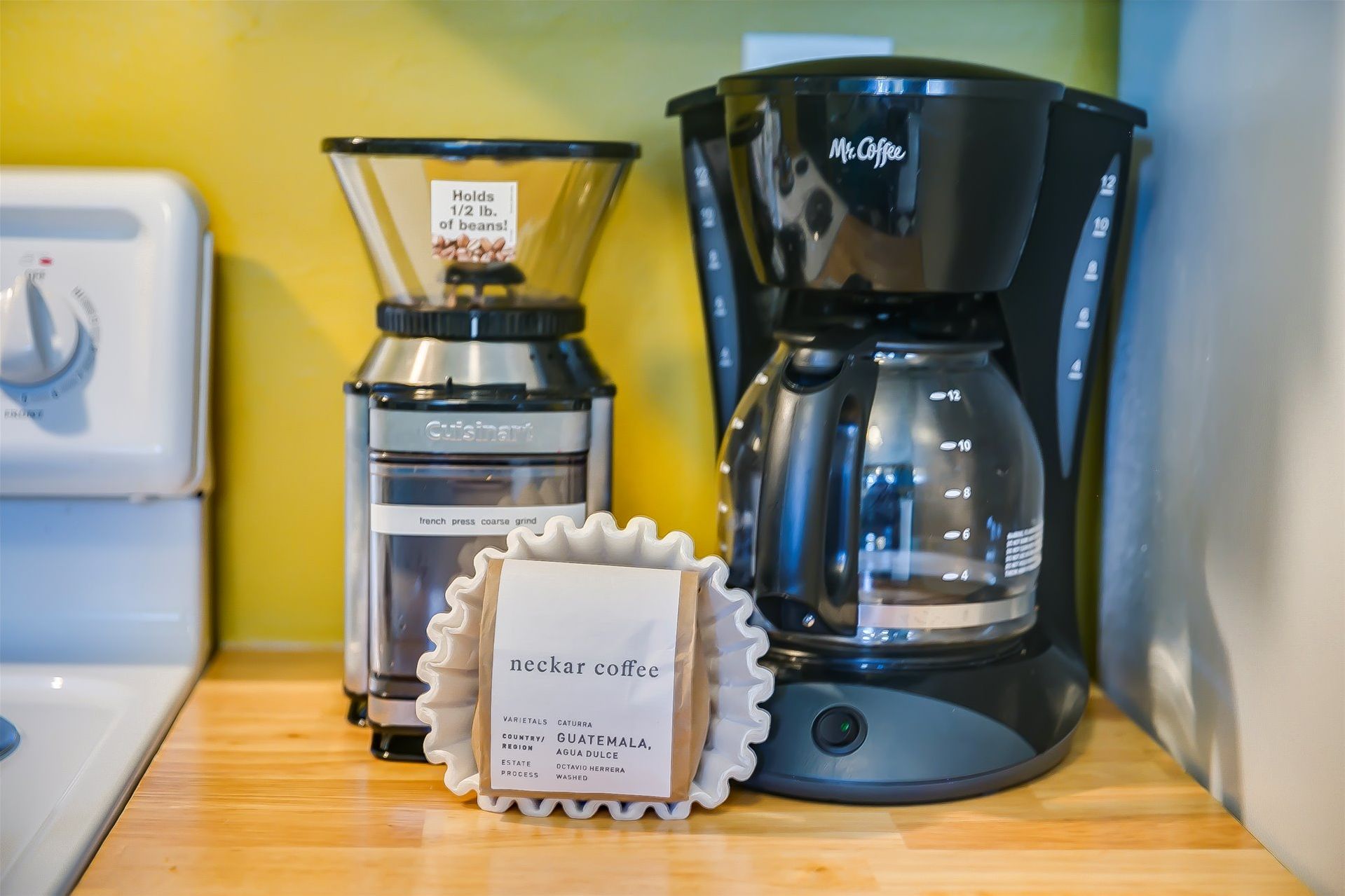 A coffee maker, a grinder, and a coffee bag on a wooden surface.