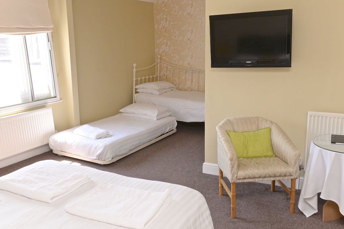 A hotel room with two beds, a chair, a table, and a TV.