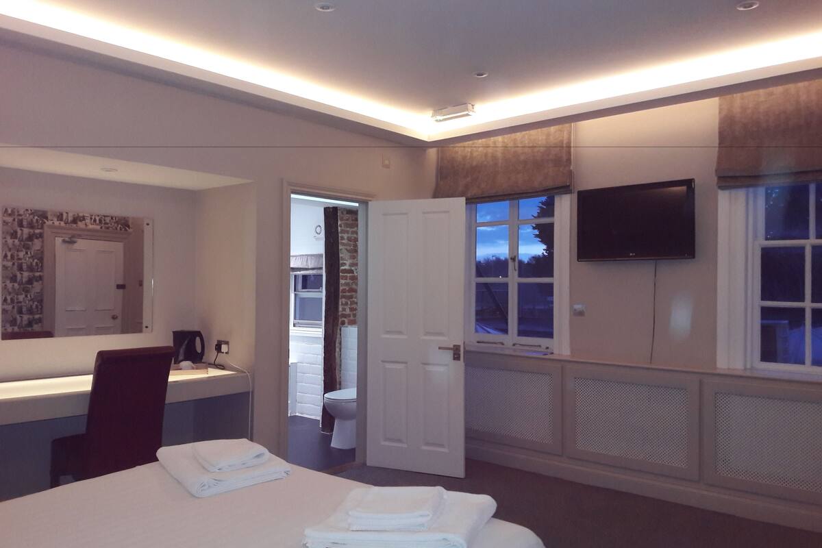 A hotel room with a bed, a TV mounted on the wall, a window with curtains, and a door leading to a balcony.