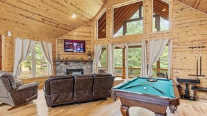 Ein gemütliches Holzhaus-Interieur mit Billardtisch, Ledersofa und Kamin aus Stein.