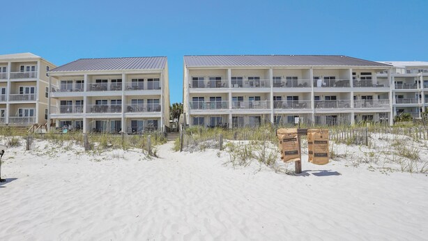 Un hotel frente a la playa con varios balcones, una playa de arena y cielo despejado.