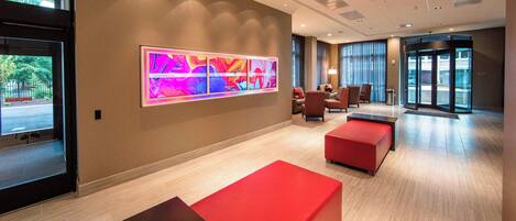 A modern lobby with a large abstract art piece, red seating, and a glass entrance.