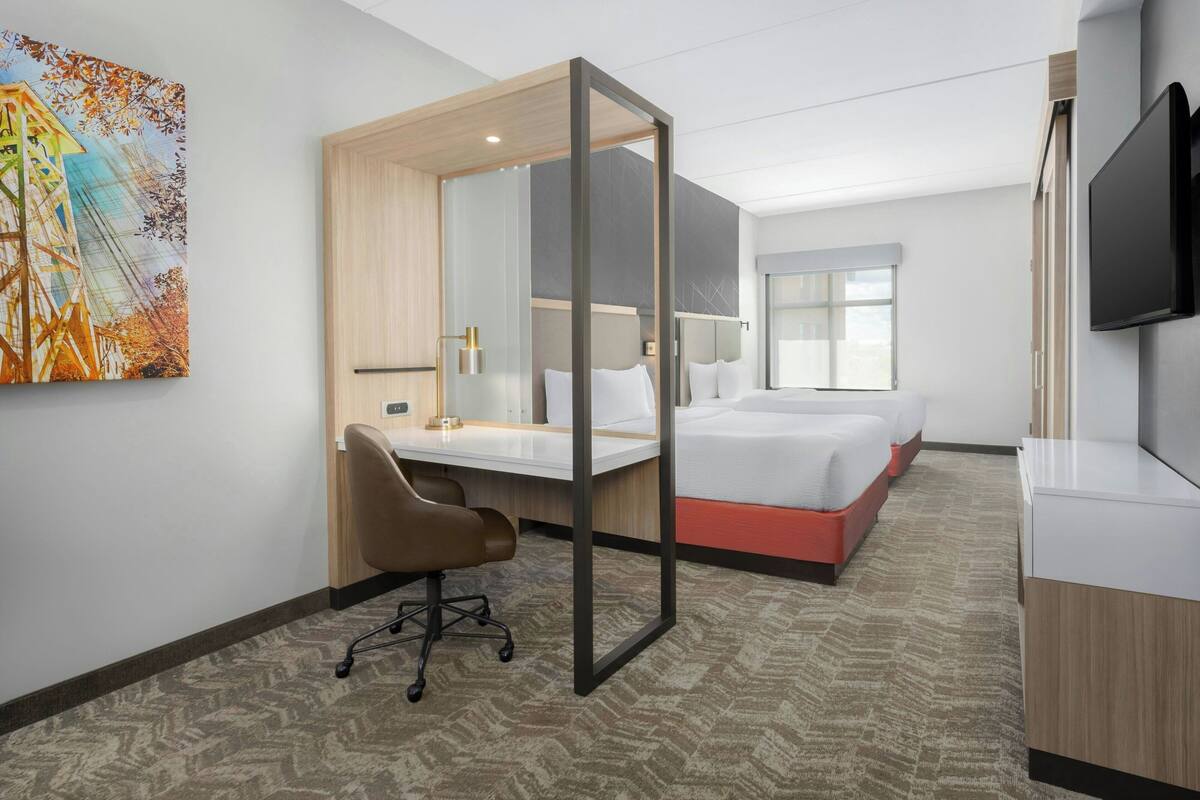 A hotel room with a bed, a desk, a chair, a TV, and a painting on the wall.