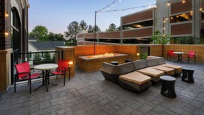 An outdoor seating area with a fire pit, red chairs, and tables, surrounded by brick walls and a modern building in the background. - SpringHill Suites by Marriott Athens Downtown/University Area (Athens)