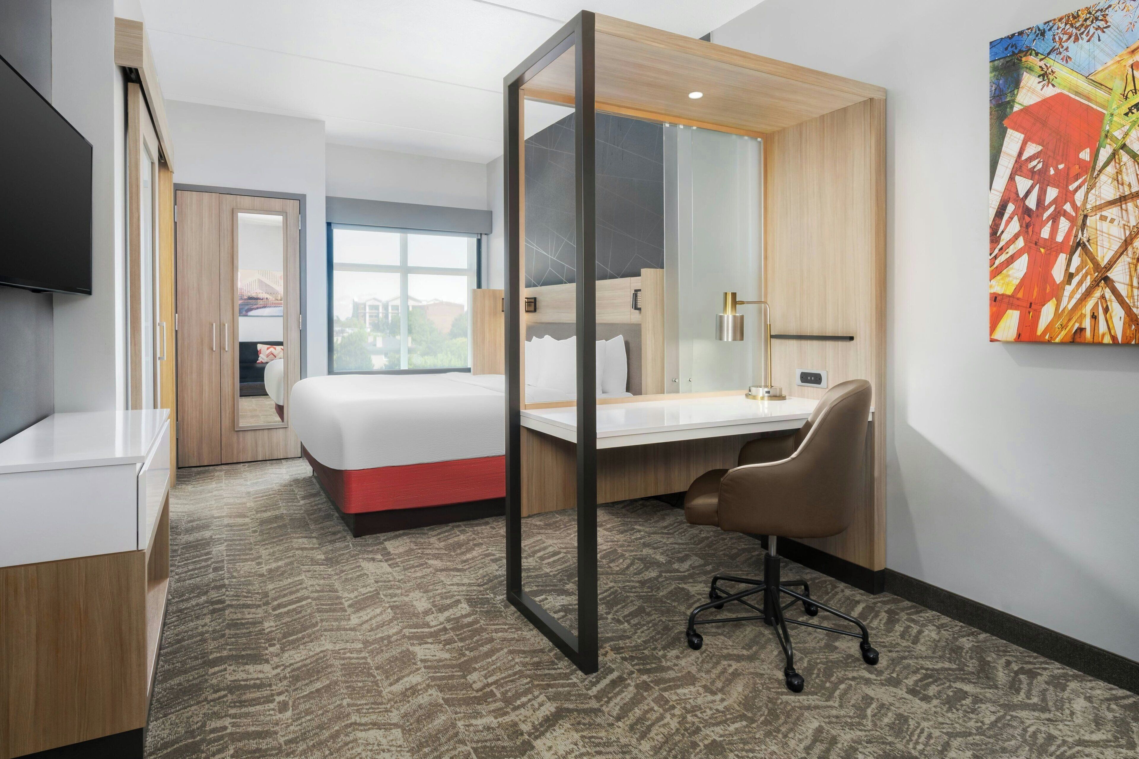 A hotel room with a bed, desk, chair, and a large window.