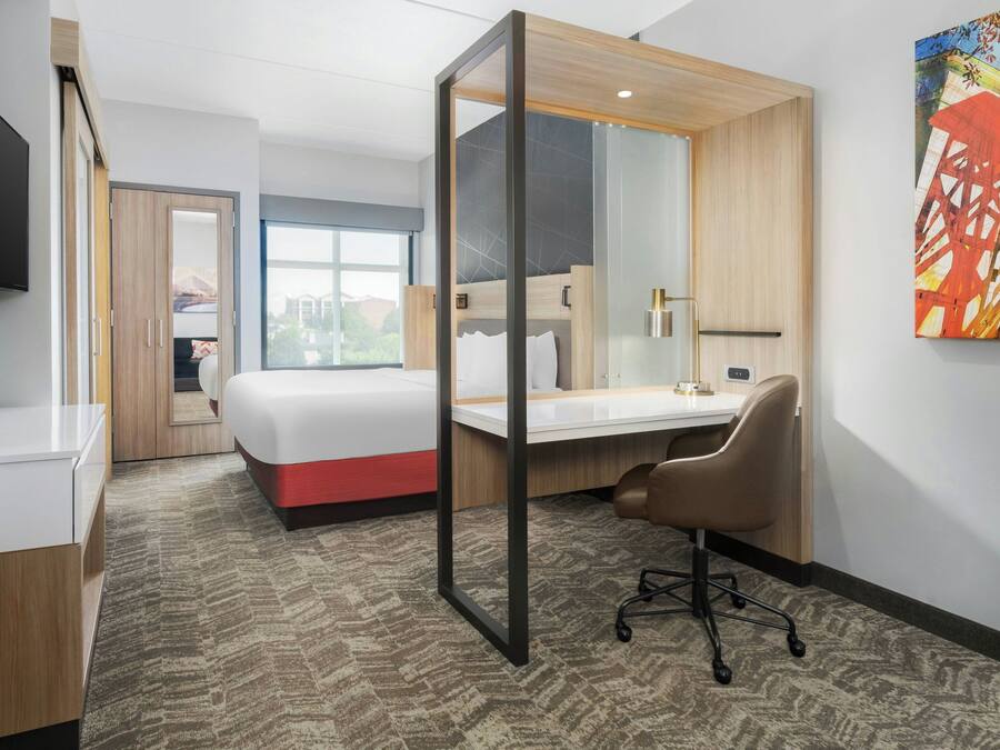 A hotel room with a bed, desk, chair, and a large window.