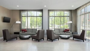 A modern living room with a sofa set, armchairs, and a coffee table. There are large windows with curtains, a flat-screen TV mounted on the wall, and a floor lamp. - SpringHill Suites by Marriott Athens Downtown/University Area (Athens)