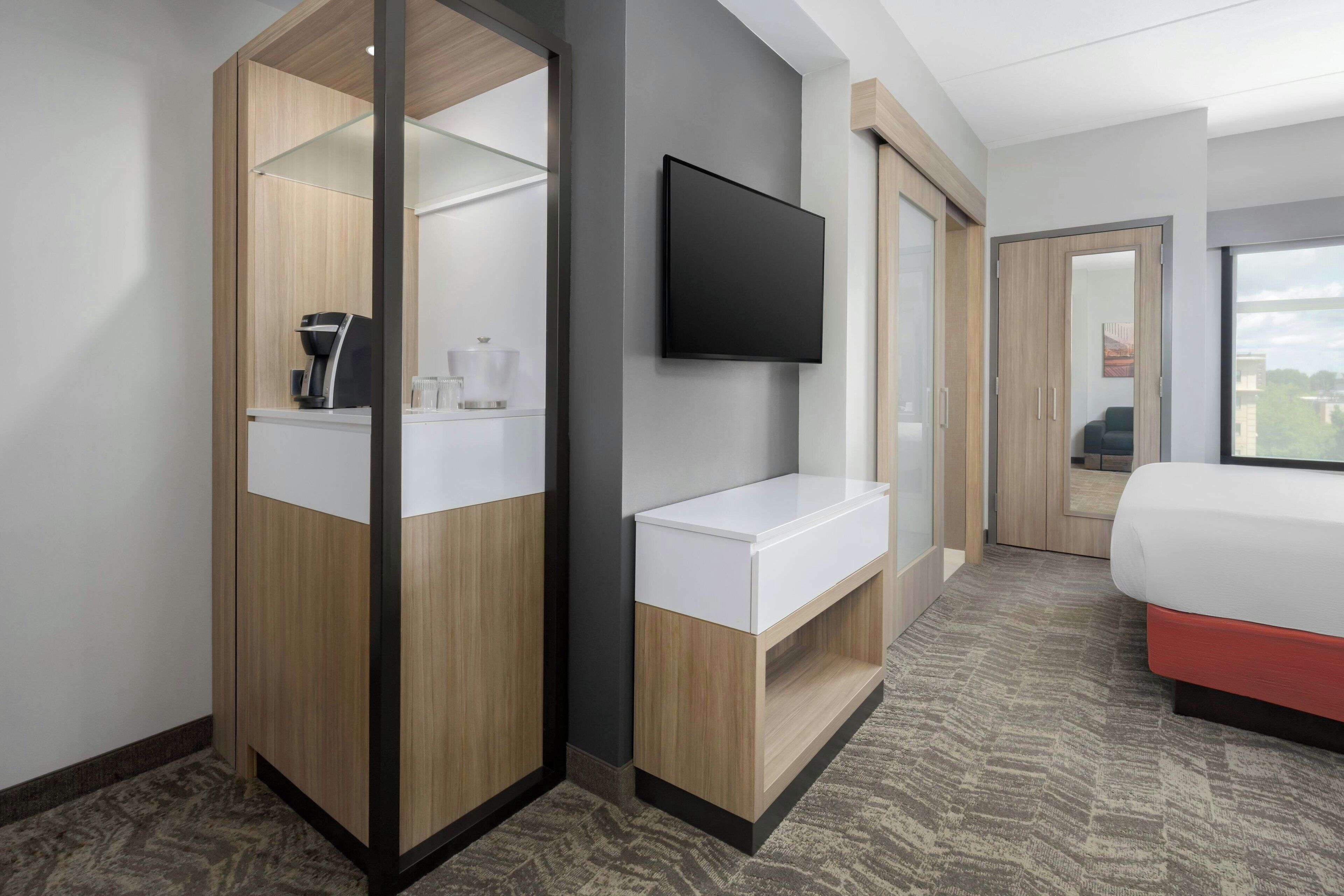 A modern hotel room with a wooden wardrobe, a flat-screen TV, a white bedside table, and a bed with a red base.