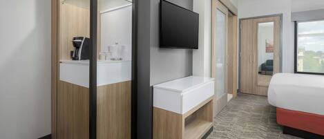 A modern hotel room with a wooden wardrobe, a flat-screen TV, a white bedside table, and a bed with a red base.