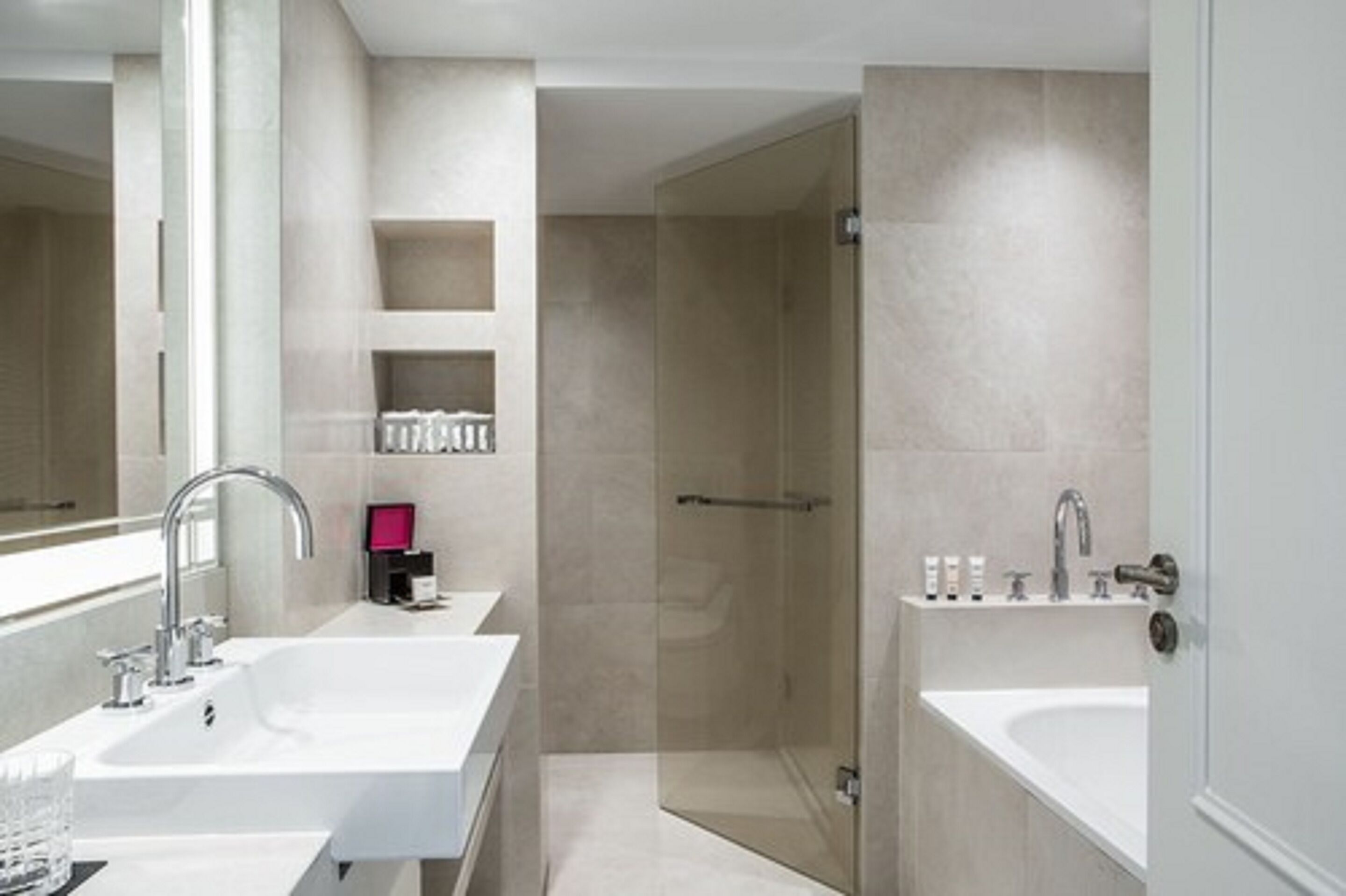 A modern bathroom with a large mirror, two sinks, a shower, and a glass-enclosed shower area.