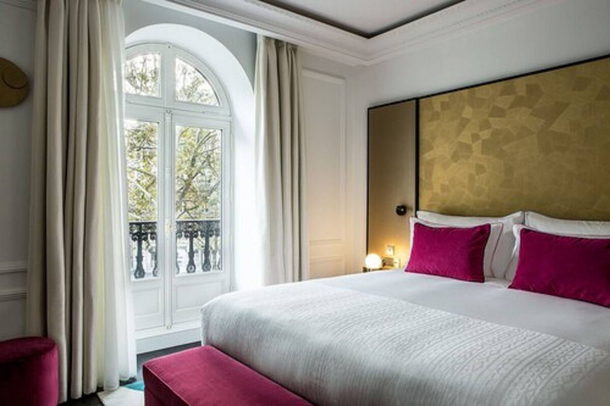 A hotel room with a large bed, a view of a balcony, and a nightstand with a lamp.