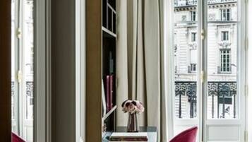 A room with a desk, a chair, a bookshelf, and a view of buildings through a window.