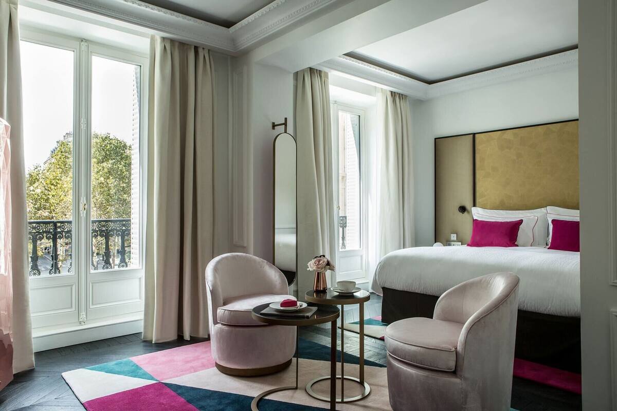 A hotel room with a bed, two armchairs, a round table, and a large mirror.