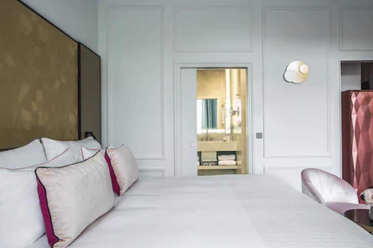 A hotel room with a large bed, a mirror, a vanity with a sink, and a shower area.
