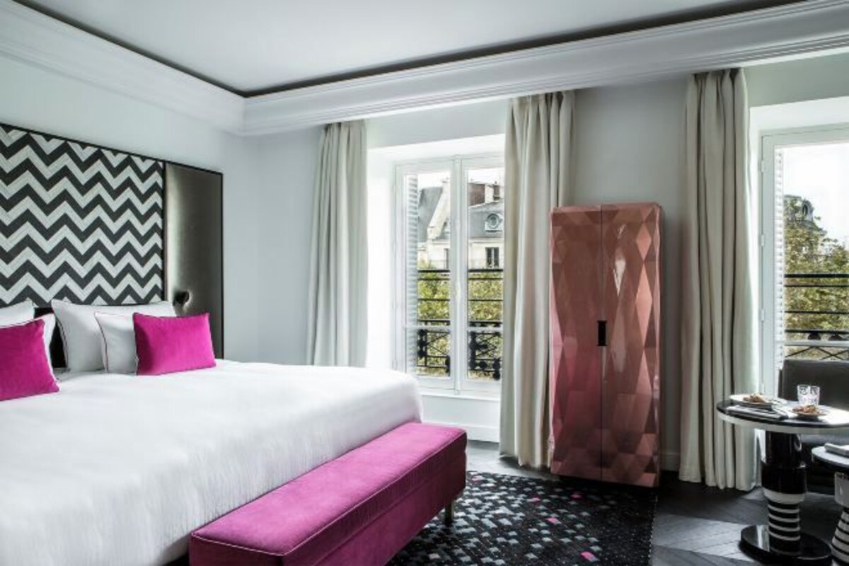 Habitación de hotel moderna con una cama grande, un banco, una mesa de comedor y vistas al exterior.