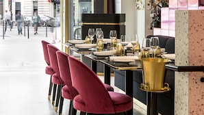 Un restaurante con una mesa larga dispuesta para comer, sillas rojas y una zona de bar de color dorado.