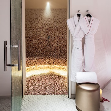 A modern bathroom with a mosaic-tiled shower area, a white bathtub, and a gold stool.