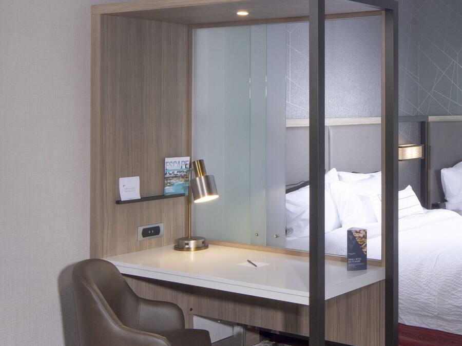 A hotel room with a desk, chair, bed, and a small trash bin.