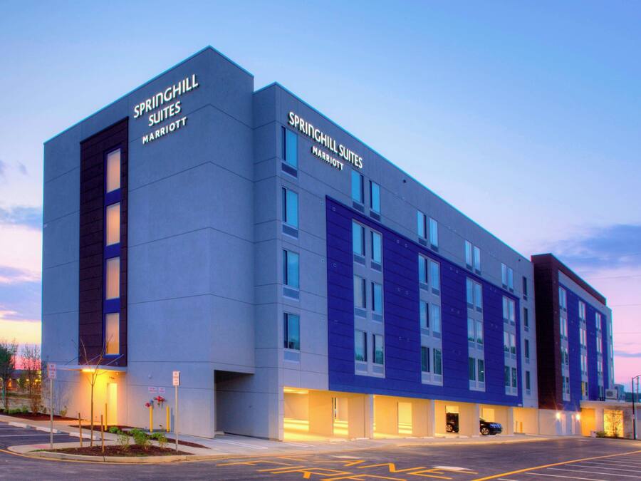 Et moderne hotel med flere suiter, store vinduer og en parkeringsplads.