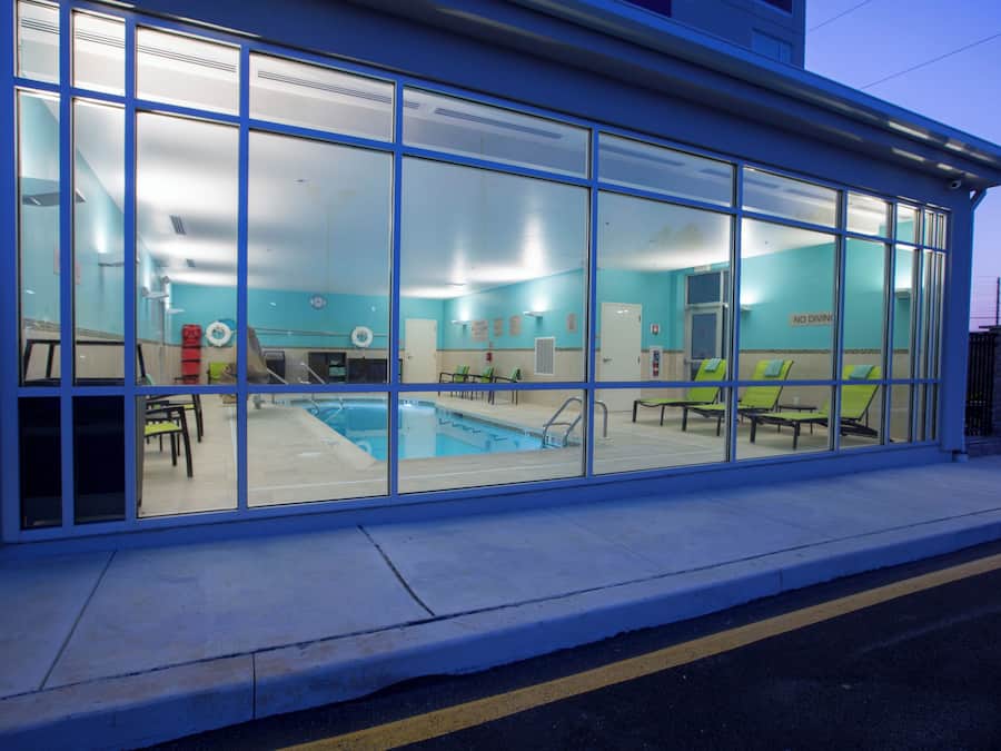 A modern building with large glass windows, a swimming pool, and lounge chairs.