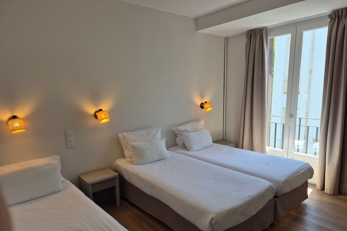A hotel room with two beds, a nightstand, and a window with curtains.