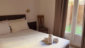 Ein ordentlich gemachtes Bett mit einem gefalteten Handtuch, ein Holzstuhl und ein Fenster mit Vorhängen.