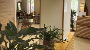 A reception area with a wooden reception desk, potted plants, and a dining area in the background. - Hôtel Bonaparte (Bastia)
