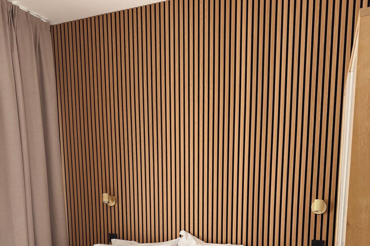 A hotel room with a bed, pillows, a bedside table with a remote, and a wall with vertical wooden slats.