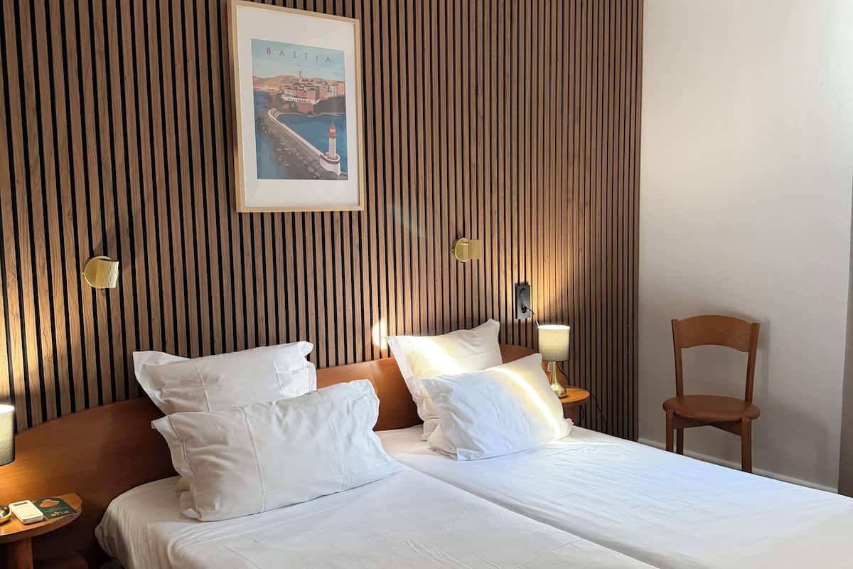 A hotel room with two beds, a wooden slat wall, a framed picture, bedside lamps, and a chair.