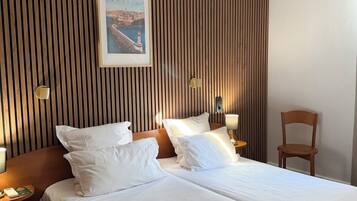 Hotelkamer met twee bedden, een wand van houten latten, een lijst met afbeelding, bedlampjes en een stoel.