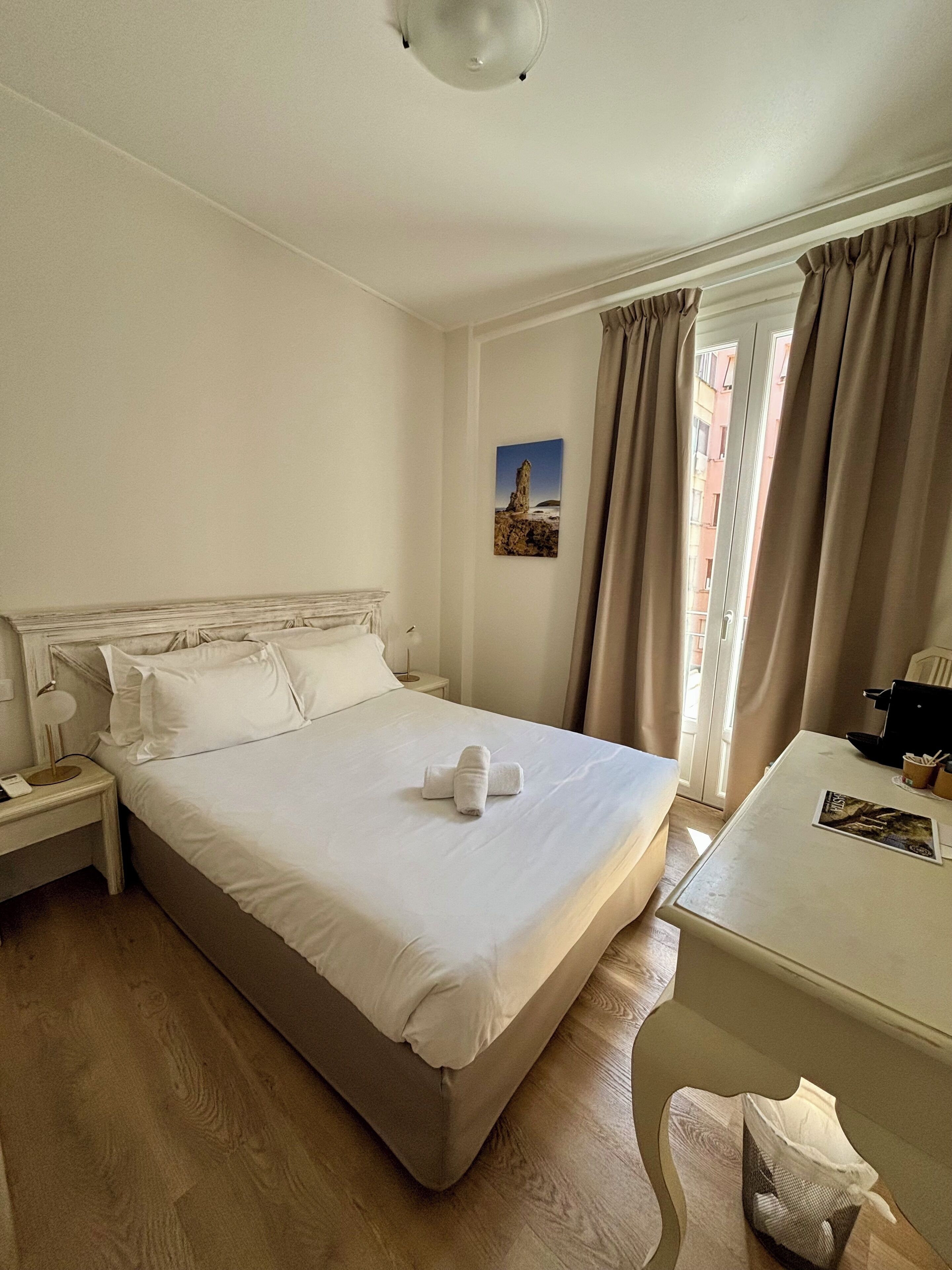 A hotel room with a large bed, a bedside table, a desk, and a window with curtains.