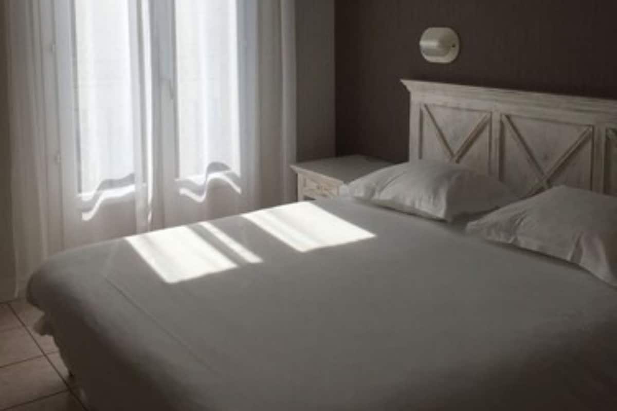 A bedroom with a bed, curtains, a nightstand, and a wall-mounted light fixture.