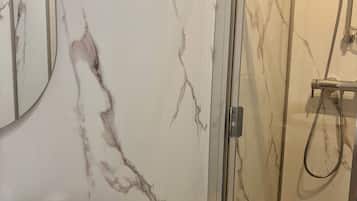 Ein modernes Badezimmer mit Marmorwand, einer begehbaren Glasdusche und einem weißen Waschbecken.