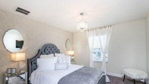 Een slaapkamer met een groot bed, twee nachtkastjes met lampen, een spiegel en een kroonluchter.