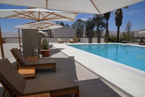 Ein Poolbereich mit Liegestühlen, Sonnenschirmen und Kübelpflanzen.