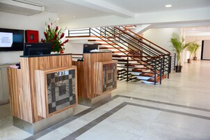 Zona de recepción de hotel con un mostrador de madera, una escalera y un televisor de pantalla plana.