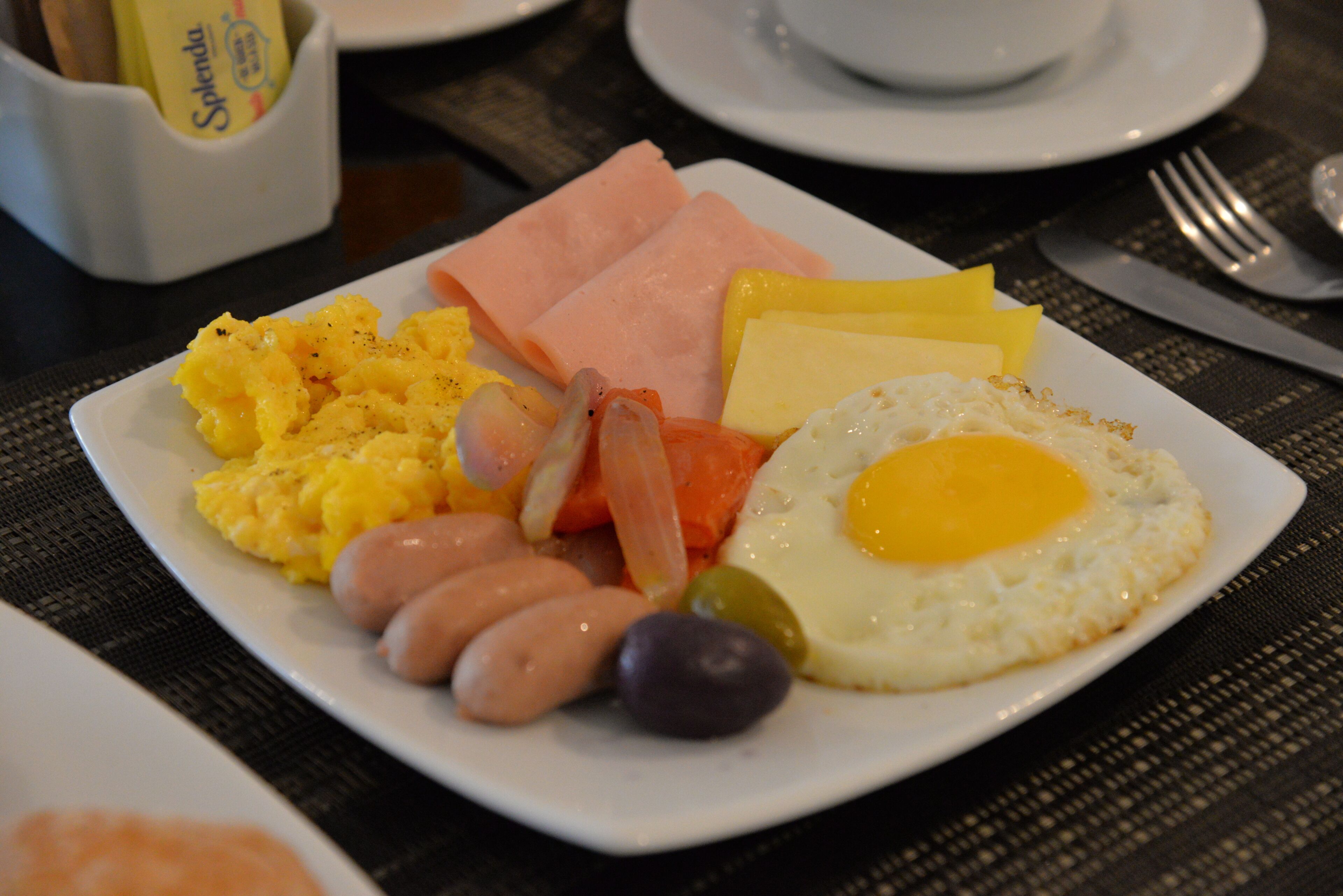 Une assiette de petit-déjeuner comprenant des œufs brouillés, du jambon, des saucisses et des légumes.