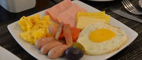 Une assiette de petit-déjeuner comprenant des œufs brouillés, du jambon, des saucisses et des légumes.