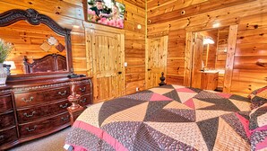 Un dormitorio de cabaña de madera con una cama grande, un aparador con varios cajones, un espejo y un televisor montado en la pared.
