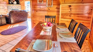 Interior de una cabaña de madera con una mesa de comedor para cuatro, un sofá de cuero y una chimenea de piedra.