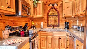 Una cocina con armarios de madera, estufa, pileta y diversos utensilios de cocina.