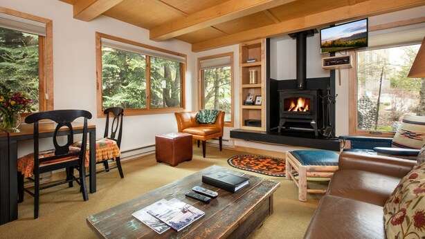 A cozy living room with a fireplace, comfortable seating, and large windows offering a view of the outdoors.