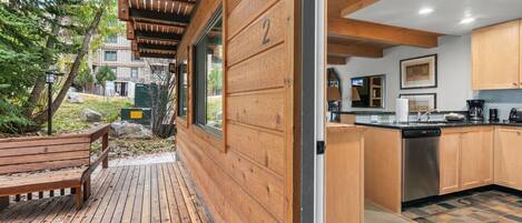 A wooden deck with a bench, a kitchen with wooden cabinets, and a view of a residential area.