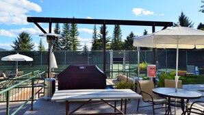 An outdoor patio with a barbecue grill, umbrellas, and seating.