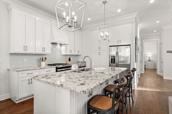 A modern kitchen with white cabinetry, a marble island, and bar stools.