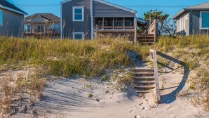 Une maison de plage dotée d’un porche couvert et d’un escalier en bois menant à une terrasse.