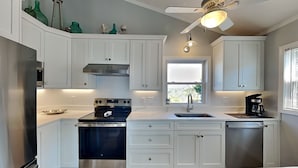 Une cuisine moderne avec des meubles blancs, un four en acier inoxydable, une machine à café et une fenêtre donnant sur un beau paysage.