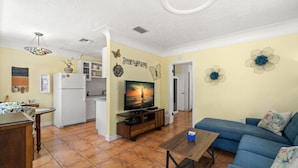 Un espacio habitable compacto con cocina, comedor y sala de estar que incluye televisor, sofá y decoración mural.