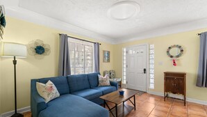 Una sala de estar con un sofá azul, una mesa de centro, una lámpara, una puerta y un mueble bajo.